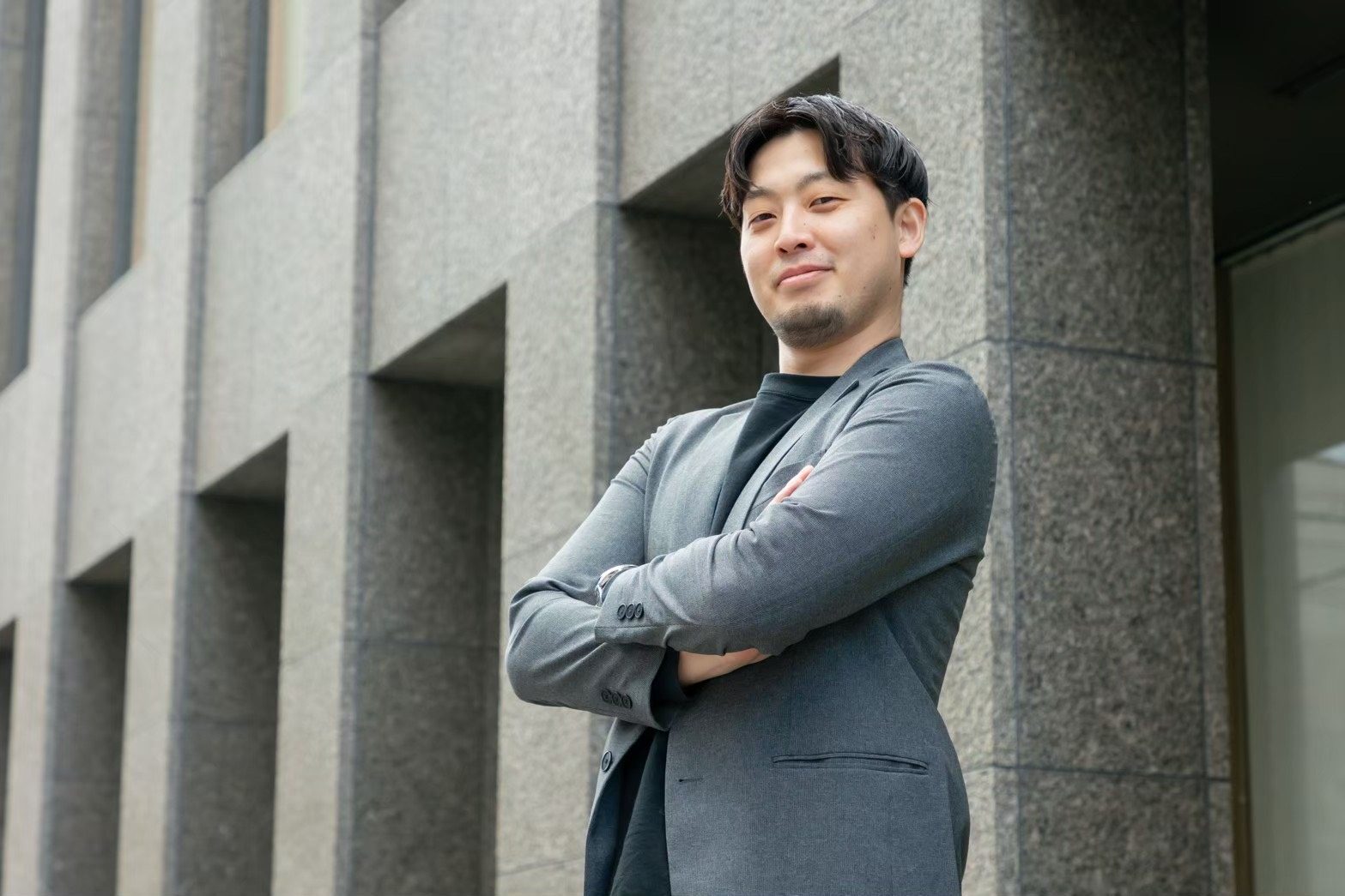 腕を組み建物を背に立つ石角太征代表取締役社長
